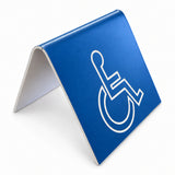 Sign Optima ATS-STD blue plastic accessibility table sign with white engraved ISA wheelchair symbol and freestanding tent-style base, studio view.