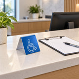 Illustrative reception-desk application of the small blue engraved plastic ATS-STD ISA table sign, 3 inches wide by 3.5 inches high by 3 inches deep.